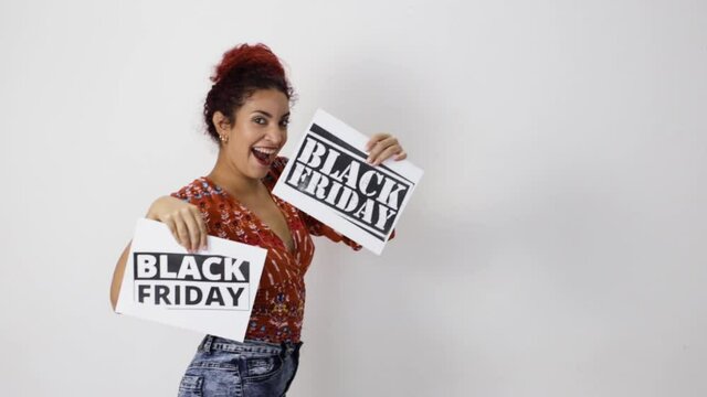 Very happy girl smiling dancing with two Black Friday posters in her hands. Young woman with white skin and curly red hair