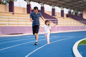 Asian little daughter is running in the stadium together with father, concept of outdoor activity, sport, exercise and competition learning for kid development.