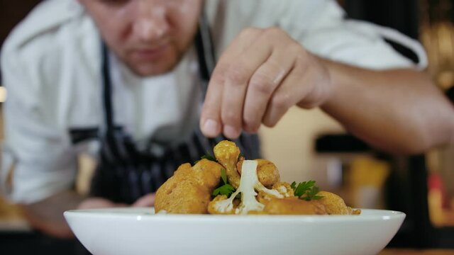 Close-up Professional Chef at Restaurant Kitchen Serves Dish Adding Final Ingredient by Hand. Cooking Vegetarian Food at Modern Home Cuisine. Delicious Fish and Chips. Preparing Meal Kitchen Slow mo