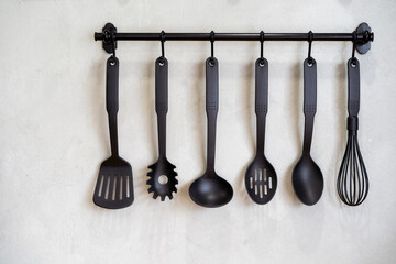 Modern kitchenware hanging on the wall rack close up. The professional kitchen tools decorate in...