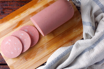 piece of whole raw pork bologna on cutting board with some slices © AGPhotography