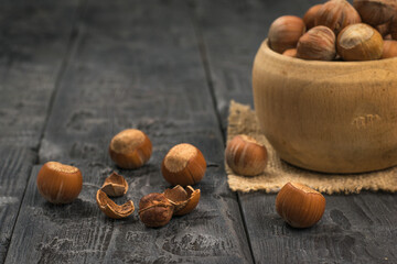 Hazelnuts in a deep wooden bowl on a black table.