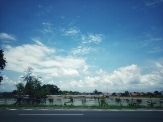 Blue cloudy sky with lake puddle water pond and urban housing below situated in highway sideway