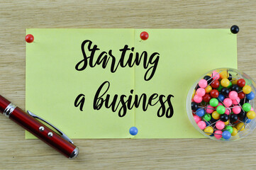Business concept. Top view of push pins, pen and memo notes written with text Starting A Business isolated on a wooden background.