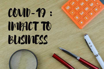 Flat lay view of calculator, pens, calculator and magnifying glass isolated on a wooden background written with text Covid-19 : Impact To Business. Business and financial concept.