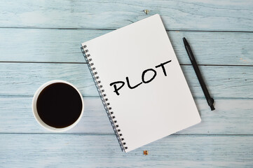 Top view of pen , a cup of coffee and notebook written with text Plot on wooden background .