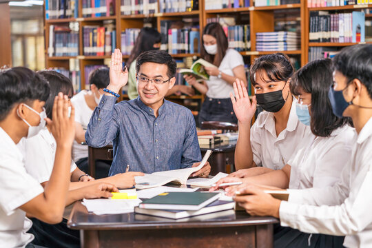 Asian teacher raising hand and Giving Lesson to group of College Students for answer question in the library and classroom, University education, back to school after reopen Covid-19 outbreak concept
