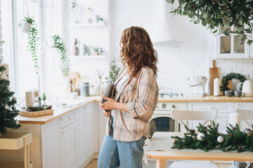 Attractive smiling woman with curly hair in plaid shirt with laptop at bright kitchen at the home, christmas time