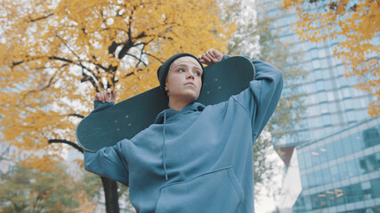 Young confident caucasian woman skater holding skateboard behind her head in the park in autumn. Low angle shot. High quality photo © CameraCraft