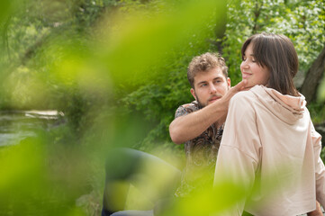 Beautiful spring or summer view through green leaves of tree near lake of lovely sweet young couple in love kissing hugging touch and looking on each other and having fun. Tenderness in relationships