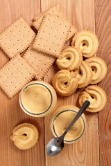 Milk pudding dessert in jar and cookies at wooden plank background. Directly Above.