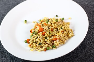 Cooked pearl barley with carrot and green peas on plate