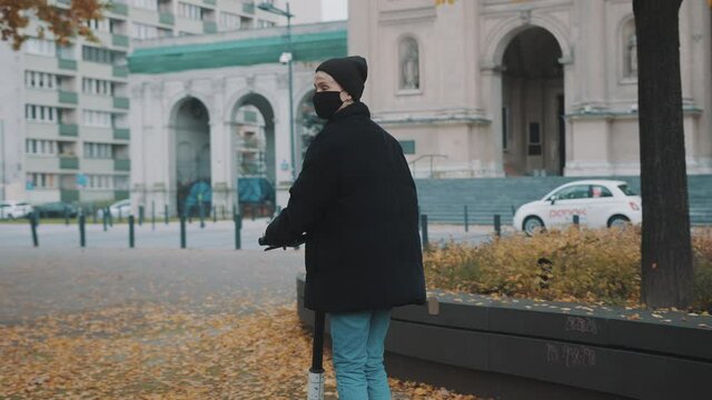 Young woman in winter black jacket with hat and face mask riding electic scooter in the city park. High quality 4k footage