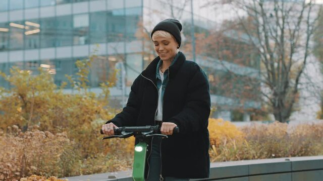 Young woman in winter black jacket with hat riding electic scooter in the city park. Ecological public transport. Concept of eco life, active lifestyle. High quality 4k footage