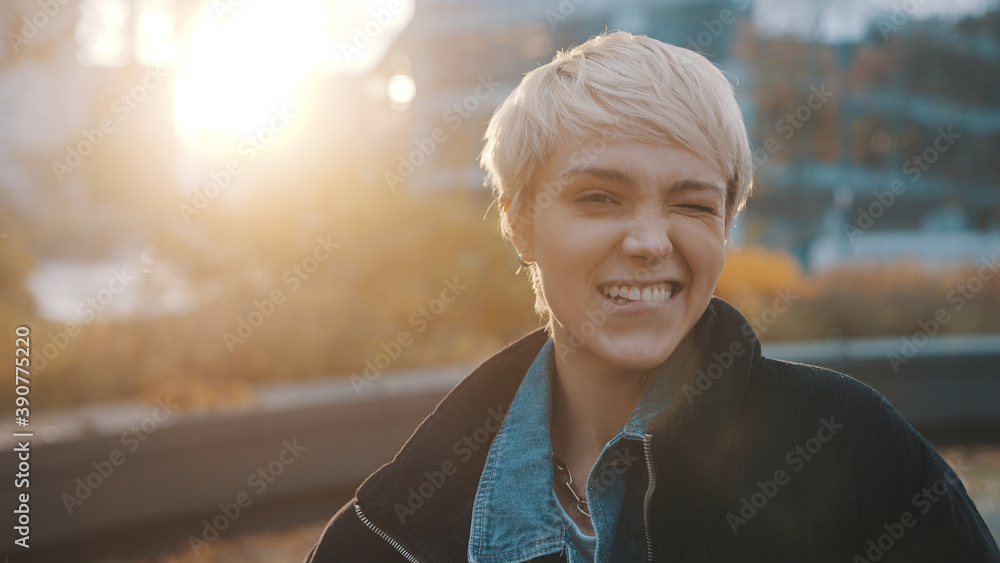 Wall mural portrait of young caucasian woman with short blond hair winking in the city park. high quality photo