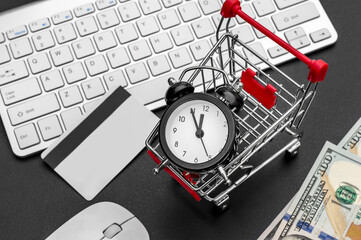 Time to shopping online. Clock with shopping cart, credit card and computer keyboard on black desk.