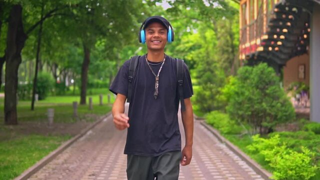 happy smiling young man with backpack listening music walking on the street slow motion lifestyle