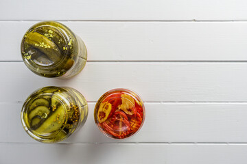 opened jars with pickled cucumbers and pepper on white wooden surface background.