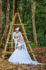 Obraz na płótnie Canvas Wedding photo shooting. The bride and groom wearing baby blue Malay traditional cloth at the forest