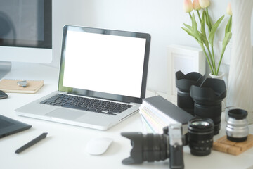 Graphic designer's or photographer workspace with laptop, computer, digital camera, digital tablet and camera accessory on white desk.