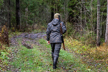 Hunter with a gun walks along a forest road	