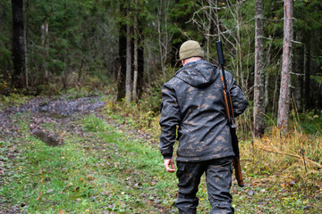 Hunter with a gun walks along a forest road	