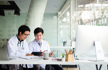 Medical team in white lab coats are sitting at a table discussing a patients records at hospital.