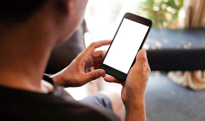 Cropped shot of young man relaxing on comfortable couch while holding smartphone with blank screen in hands.