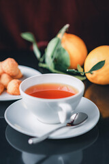 White glass cup with black, red tea with lemon on a dark glass table.
