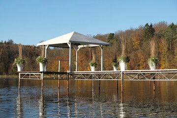 Moody landscape with wooden pier with white gazebo over a lake surrounded by forest in autumn...