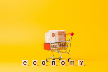 A shopping cart filled with a five-thousand-ruble bill. There are wooden cubes with the text...