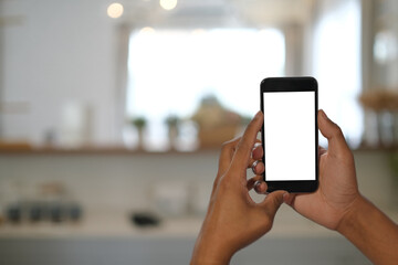 Mockup image of man hands holding mobile phone with blank screen on on blur kitchen background.