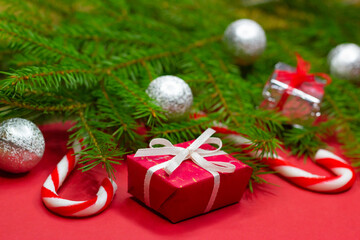 Fototapeta na wymiar Close-up of branches of christmas tree decorated with gift boxes, christmas balls and candy canes on red background