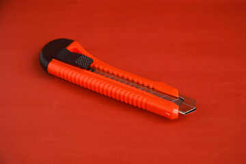 Red cutter knife on red background, sharp knife stationery