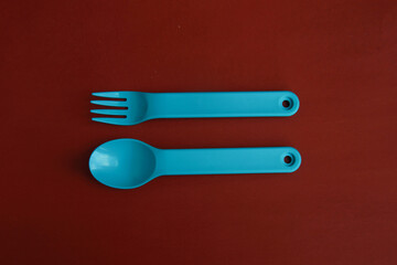 plastic blue spoon and fork for baby on red background