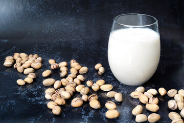 Vegetable pistachio milk in a glass stands on a dark background. Pistachio nuts in shells are...