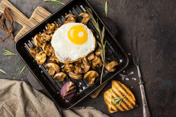 Fried egg and mushrooms on grill pan with onion, rosemary, bread