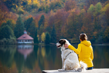 Woman sitting with a dog on dock at the autumn lake