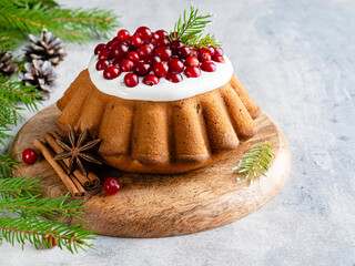 Christmas orange cake with dried cranberry, cinnamon and anise star covered by white icing cream and fresh berries. Cake on wooden plate. Christmas and new year background. Fir branches. Copy space