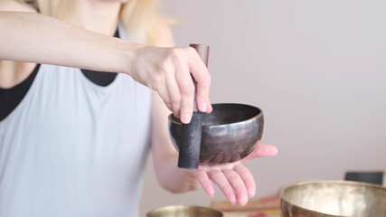 Woman playing on Tibetan singing bowl while sitting on yoga mat. Vintage tonned.