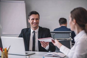 Man in tie taking folder from long-haired woman.