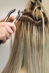 Obraz premium master makes hair extensions to a woman. Close-up of the process. Vertical photo