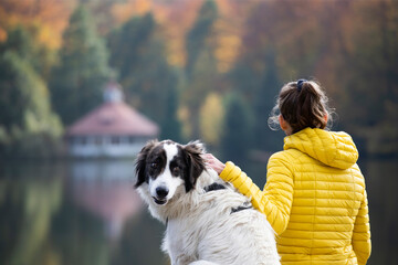 Woman sitting with a dog on dock at the autumn lake