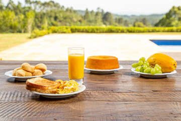 Rusted table with breakfast, with fruits, water and papaya. A plate of toast and eggs, orange juice with cornmeal cake.