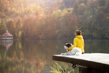 Woman sitting with a dog on dock at the autumn lake