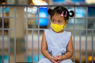 Cute little girl wearing protection face mask sitting at shopping mall.