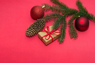 Natural spruce tree branch with a fir cone and Christmas decorations on a red background. Merry christmas and New Year. A minimalist composition, celebration and giving gifts. Copy space, flat lay.