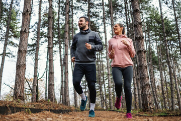 Full length of fit couple running trough woods at autumn and preparing for marathon.