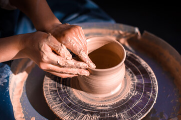 Fototapeta na wymiar Women hands. Potter at work. Creating dishes. Potter's wheel. Dirty hands in the clay and the potter's wheel with the product. Creation. Working potter.