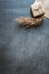 Gift box wrapped in craft paper with a reed stalk, dried pampas grass on a dark background. New fashionable home decor, copy space. Vertical photo.